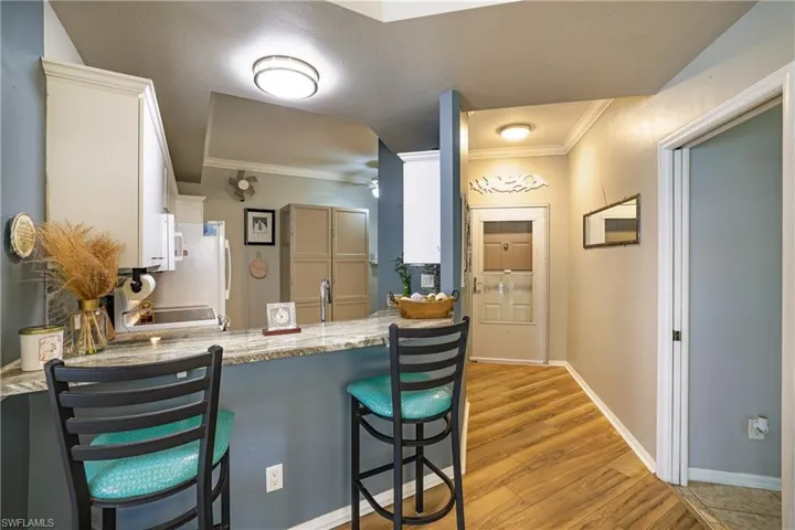 Kitchen with a kitchen bar, white cabinets, crown molding, light wood-type flooring, and light stone countertops