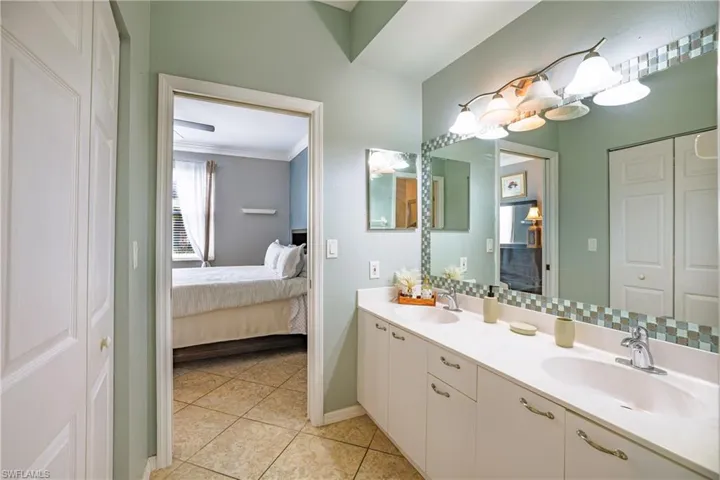 Ensuite bathroom with double vanity, ornamental molding, light tile patterned floors, and a closet