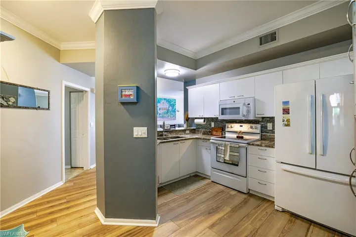 Kitchen with white appliances, light wood-style flooring, white cabinets, crown molding, and tasteful backsplash