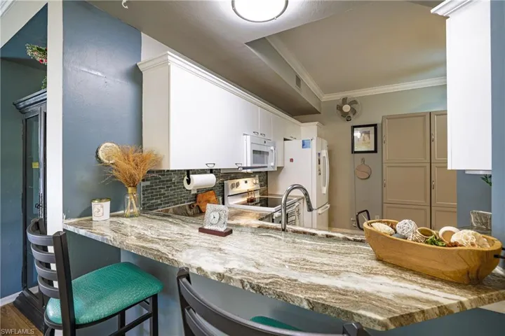 Kitchen featuring backsplash, white cabinets, a kitchen bar, white appliances, and a peninsula