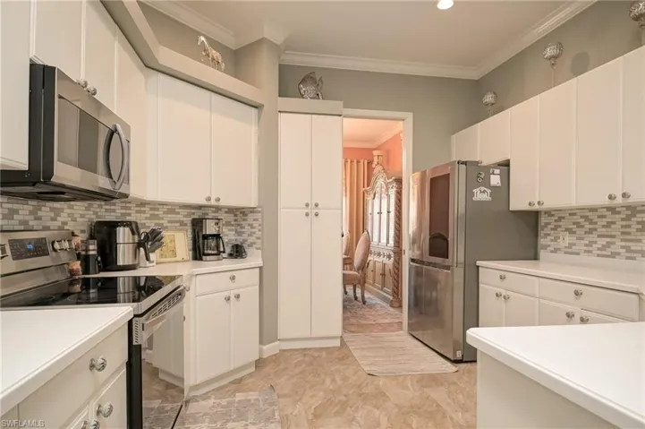 Kitchen with stainless steel appliances, crown molding, backsplash, light countertops, and white cabinets