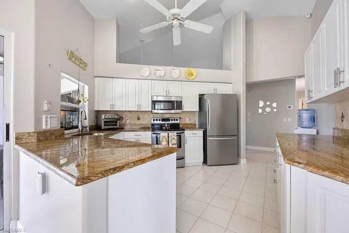 Kitchen featuring high vaulted ceiling, white cabinets, kitchen peninsula, and stainless steel appliances