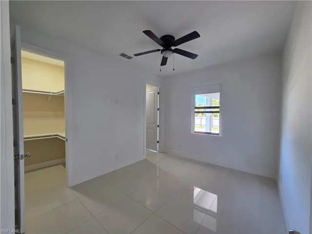Unfurnished bedroom featuring a ceiling fan, a spacious closet, and light tile patterned floors