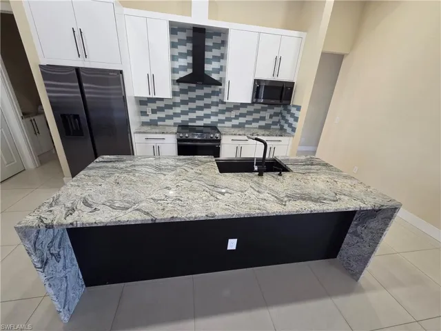 Kitchen with light stone counters, light tile patterned floors, refrigerator with ice dispenser, and white cabinets