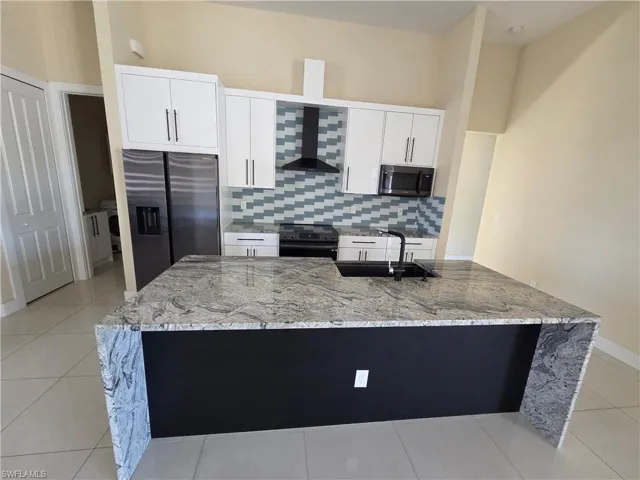 Kitchen featuring light stone countertops, light tile patterned floors, stainless steel appliances, and white cabinets