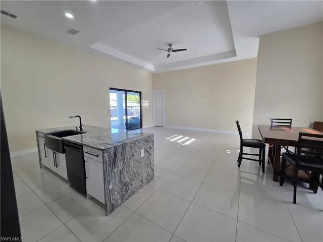 Kitchen featuring light stone counters, a raised ceiling, light tile patterned floors, open floor plan, and a center island with sink