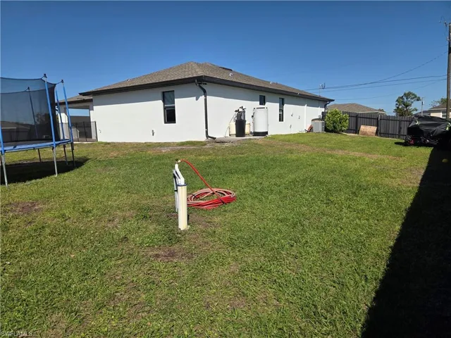 Back of house with a fenced backyard, stucco siding, a trampoline, and a shingled roof