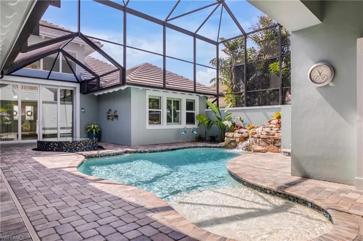 View of pool featuring deck space, a waterfall, spa, and an entirely screened enclosure.