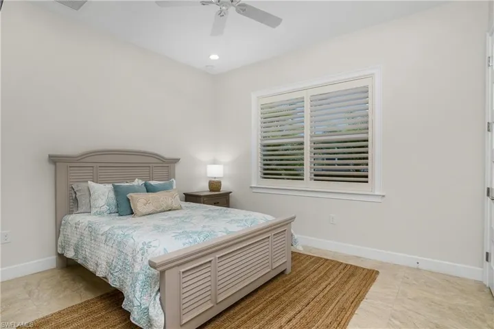 Main house guest Bedroom, features tile flooring, plantation shutters, ceiling fan.