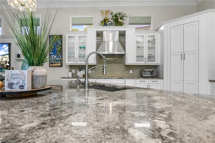 Luxury surfaces... Kitchen with stone countertops, tasteful backsplash, sink, and white cabinets.