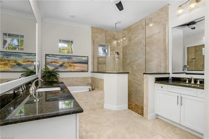 Luxurious master Bathroom with separate vanities, crown molding, independent shower and bath, ceiling fan, framed mirrors.