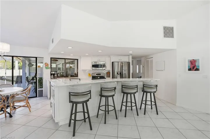 Kitchen with a breakfast bar area, white cabinets, stainless steel appliances, light stone countertops, and light tile patterned flooring