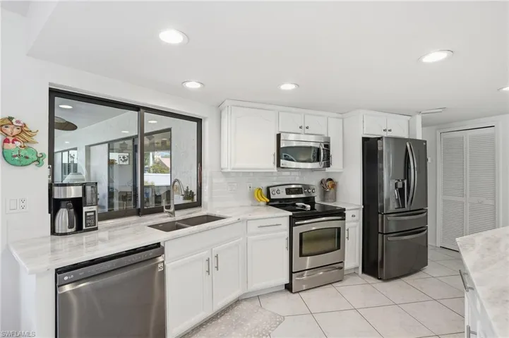 Kitchen featuring appliances with stainless steel finishes, white cabinetry, light tile patterned floors, decorative backsplash, and light stone counters