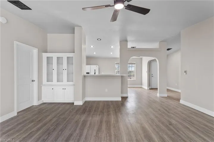 Unfurnished living room featuring arched walkways, dark wood-style flooring, ceiling fan, and recessed lighting