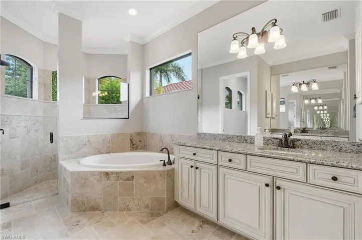 Spacious bathroom featuring a built-in soaking tub, a separate glass-enclosed shower, dual vanity with a granite-style countertop, and arched windows