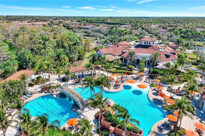 Expansive resort-style pool area featuring multiple swimming pools, a decorative bridge, and abundant lounge seating with orange umbrellas