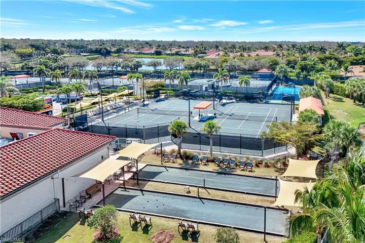 Recreational area featuring multiple tennis courts, two bocce ball courts with shade structures, and an adjacent building with a red tile roof