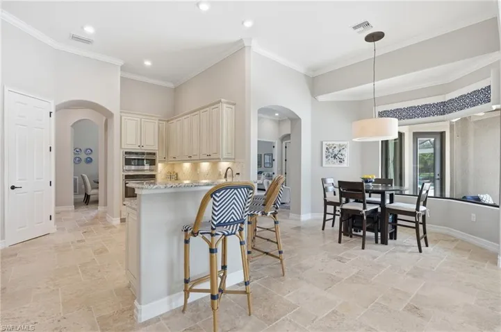 Spacious kitchen and dining area featuring light-toned tile flooring, recessed lighting, crown molding, a built-in oven and microwave, and a counter-height breakfast bar