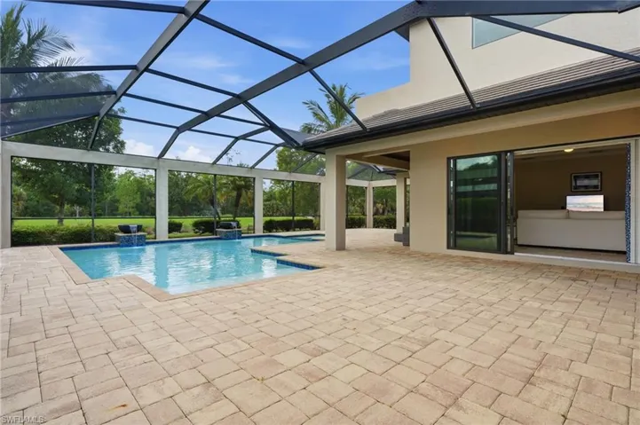 Screened outdoor living space featuring a swimming pool with integrated water features, expansive paver patio, and sliding glass doors opening to interior