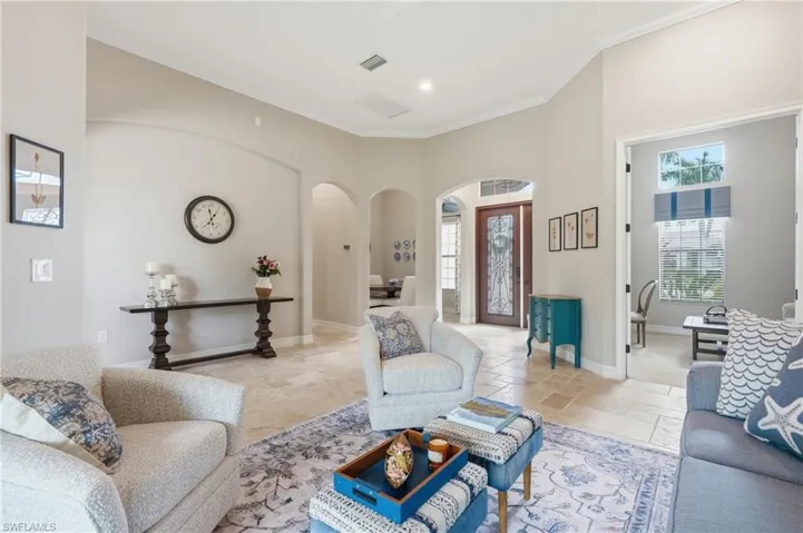 Spacious living area featuring light-toned tile flooring, vaulted ceilings, and crown molding