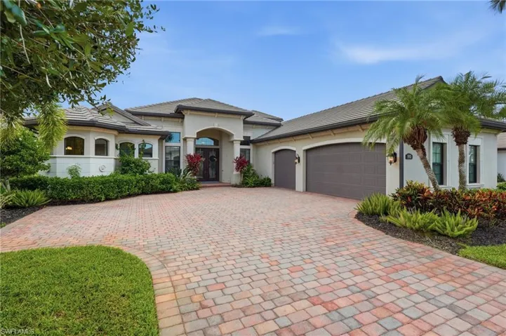 Expansive paver driveway leading to a stucco exterior with a tile roof