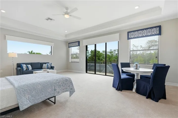 Spacious room featuring neutral carpeting, a tray ceiling with recessed lighting and a ceiling fan, a large window, and sliding glass doors to a balcony