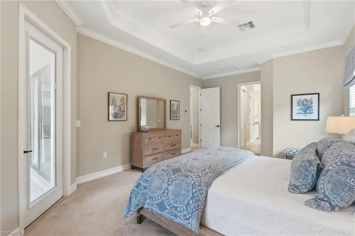 Carpeted interior space featuring a tray ceiling with crown molding, a ceiling fan, and a glass-paneled door