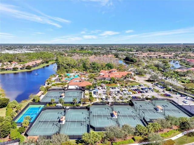 Expansive community grounds featuring multiple tennis courts, a large clubhouse with a terracotta tile roof, and a significant body of water