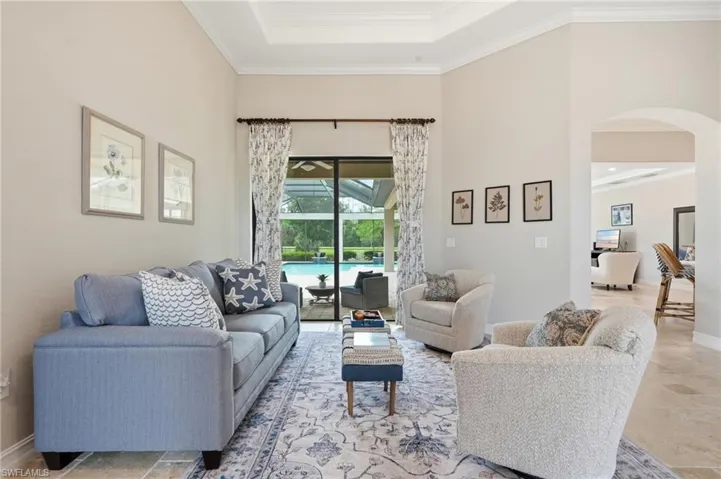 Travertine-style tile flooring throughout this living area with a tray ceiling and crown molding