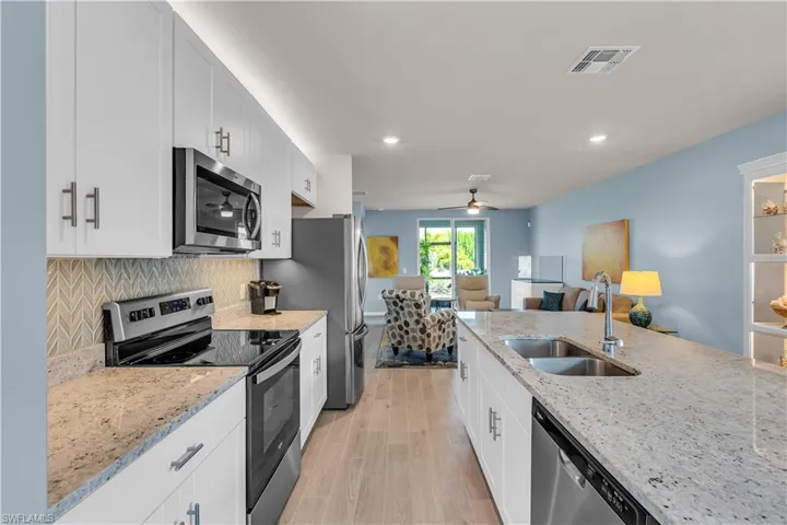 Kitchen featuring stainless steel appliances, open floor plan, light stone counters, light ceramic tile floors, and Blue and Gray tasteful backsplash. Under counter and recessed lighting.