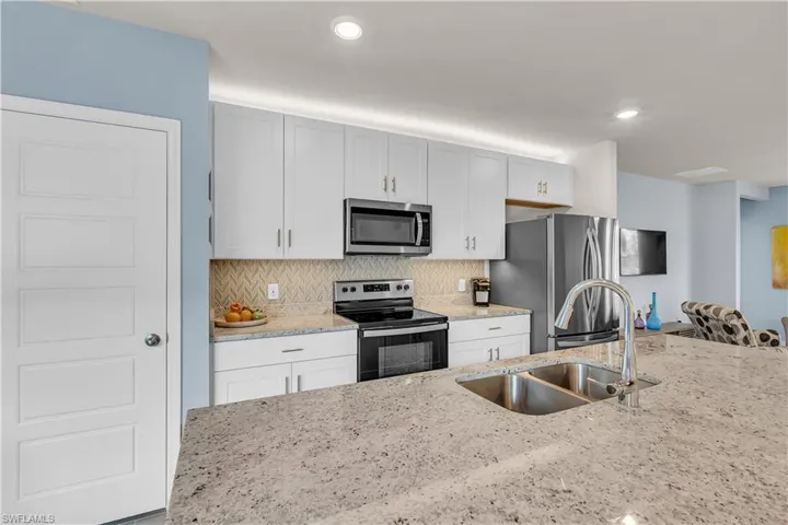 Kitchen featuring appliances with stainless steel finishes, light stone countertops, decorative backsplash, recessed lighting, and white cabinetry