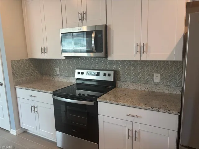 Kitchen with appliances with stainless steel finishes, light stone counters, white cabinets, and tasteful Blue/Gray decorative backsplash