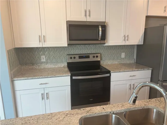 Kitchen featuring appliances with stainless steel finishes, light stone counters, white cabinetry, and decorative Blue and Gray decorative backsplash