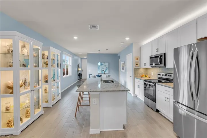 Kitchen with stainless steel appliances, light stone countertops, decorative Blue and Gray backsplash, a kitchen bar, and a kitchen island with sink