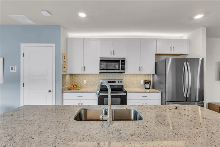 Kitchen featuring stainless steel appliances, Blue and Gray decorative backsplash, light stone counters, large pantry and recessed lighting