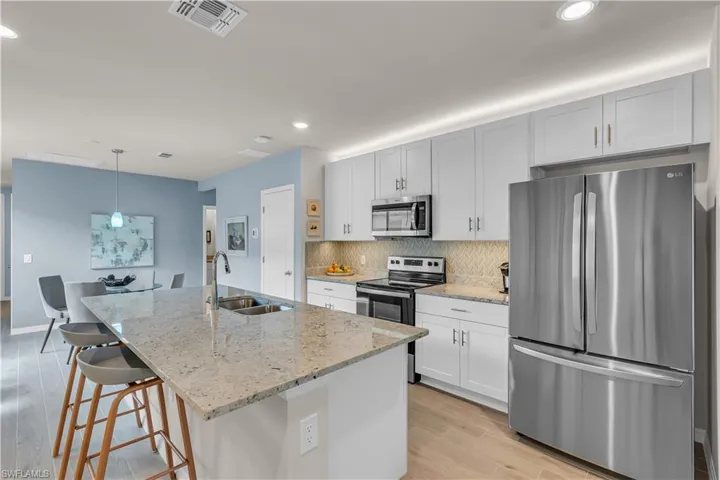 Kitchen with appliances with stainless steel finishes, light stone counters, tasteful Blue and Gray decorative backsplash, recessed lighting, and light ceramic tile floors