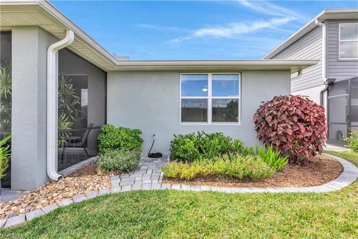 View of back of home with stucco siding, a enclosed lanai/patio and a yard beautifully landscaped with flowers and colorful schrubs.