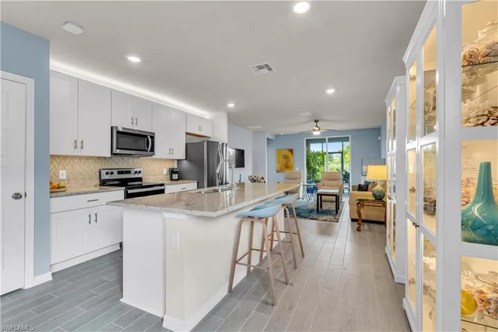 Kitchen featuring light stone countertops, an island with sink, a breakfast bar, tasteful Blue and Gray backsplash, ceramic Tile floor and stainless steel appliances