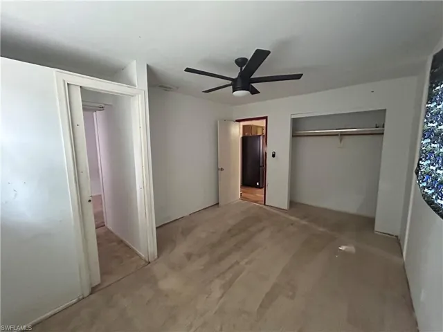 Unfurnished bedroom featuring a closet, light colored carpet, a ceiling fan, and freestanding refrigerator