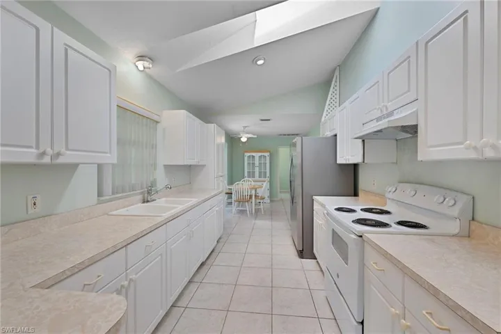 Kitchen with white electric range oven, white cabinets, under cabinet range hood, lofted ceiling, and light countertops