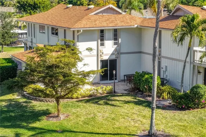 Back of property featuring a shingled roof, a lawn, and stucco siding
