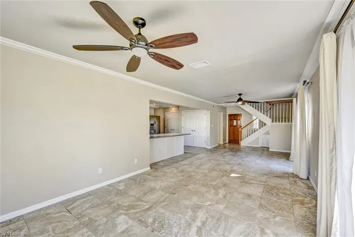 Unfurnished living room featuring stairway, a ceiling fan, and crown molding