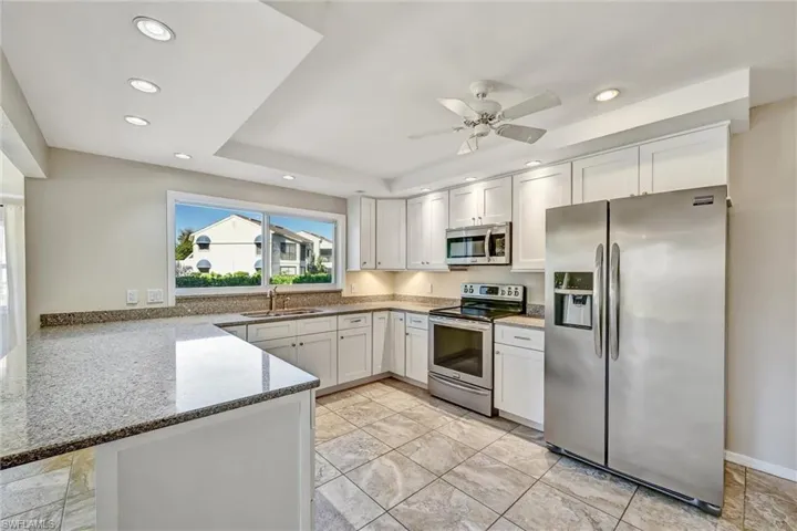 Kitchen with stainless steel appliances, light stone countertops, white cabinetry, a peninsula, and recessed lighting