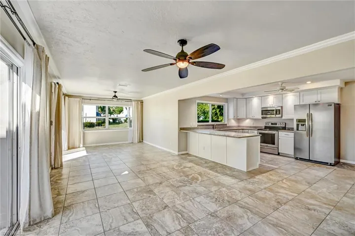 Kitchen featuring ceiling fan, stainless steel appliances, white cabinetry, open floor plan, and a peninsula