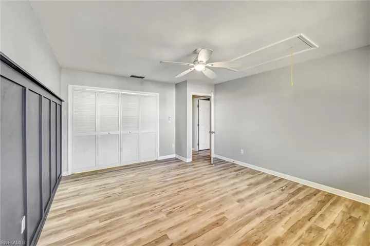 Unfurnished bedroom with attic access, a closet, light wood finished floors, and a ceiling fan