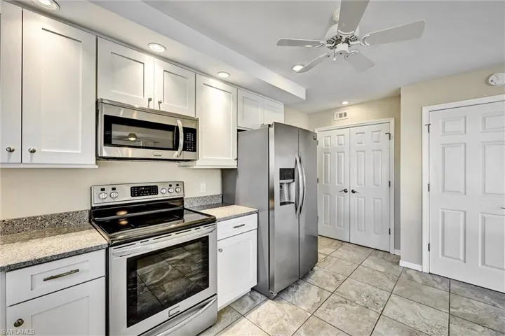 Kitchen with appliances with stainless steel finishes, white cabinetry, light stone countertops, recessed lighting, and ceiling fan