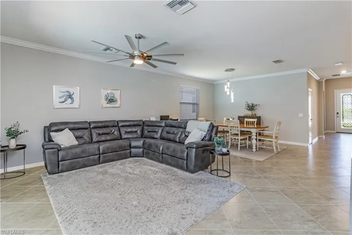 Living room with crown molding, ceiling fan, and light tile patterned floors