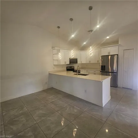 Kitchen with white cabinetry, stainless steel appliances, vaulted ceiling, a peninsula, and pendant lighting