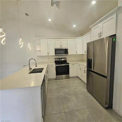 Kitchen featuring lofted ceiling, stainless steel appliances, white cabinetry, a peninsula, and light stone countertops