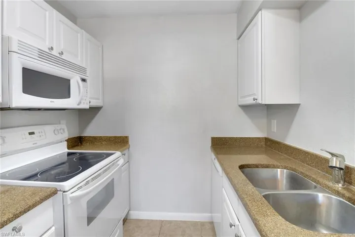 Kitchen featuring a sink, white cabinetry, white appliances, light tile patterned flooring, and baseboards